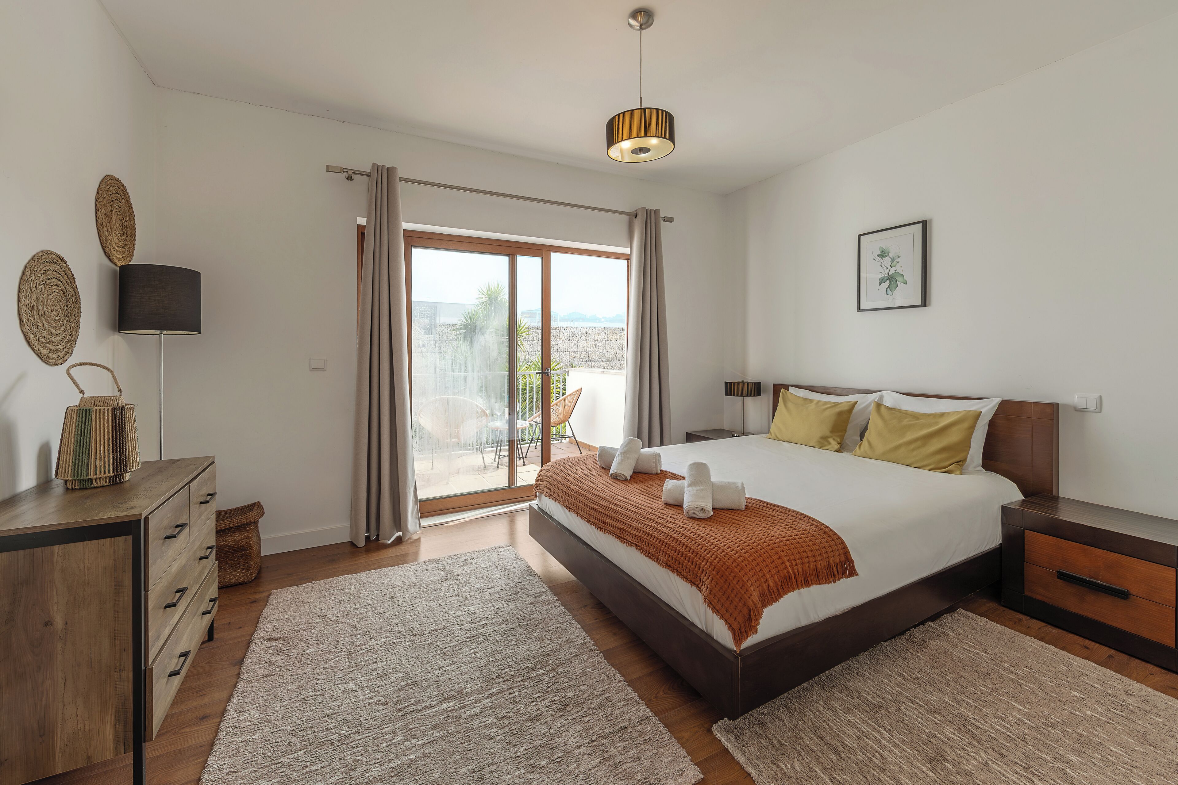 A bedroom with a bed, bedside tables, a lamp, a view through a glass door, and a ceiling light.