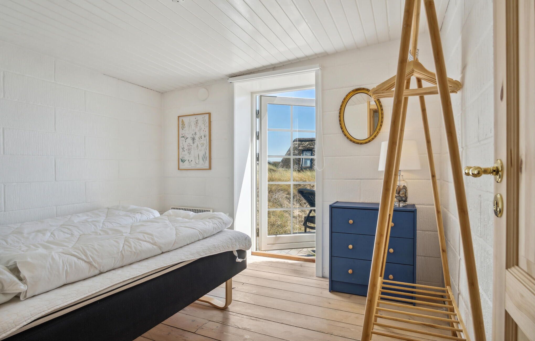 A bedroom with a bed, a dresser, a ladder, and a window leading to an outdoor area.