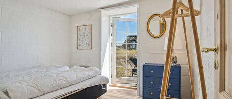 A bedroom with a bed, a dresser, a ladder, and a window leading to an outdoor area.