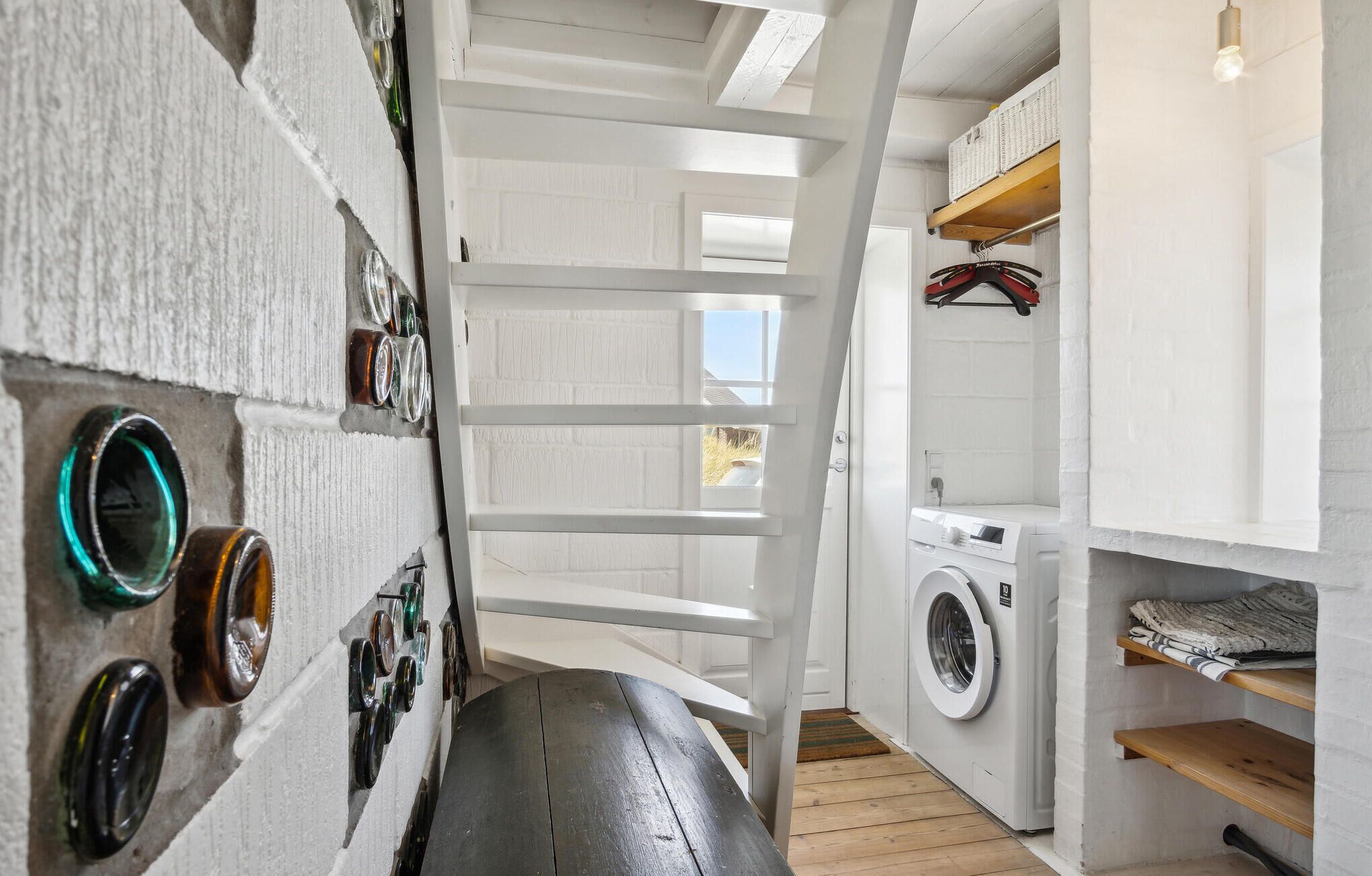 A laundry room with a washing machine, shelves with folded clothes, and a wooden bench.