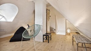 A spacious attic room with a sloped ceiling, a large window, a green chair, a small table, and a wooden bench. - 3 bedroom gorgeous home in Blåvand (Blåvand)