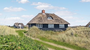 A traditional thatched-roof house with a small porch and a chimney, surrounded by grassy fields and a clear sky. - 3 bedroom gorgeous home in Blåvand (Blåvand)