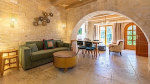 Ein gemütliches Interieur mit einer Steinsäule, einem grünen Sofa, einem runden Korbstuhl und einem Holzespeisetisch mit Stühlen.