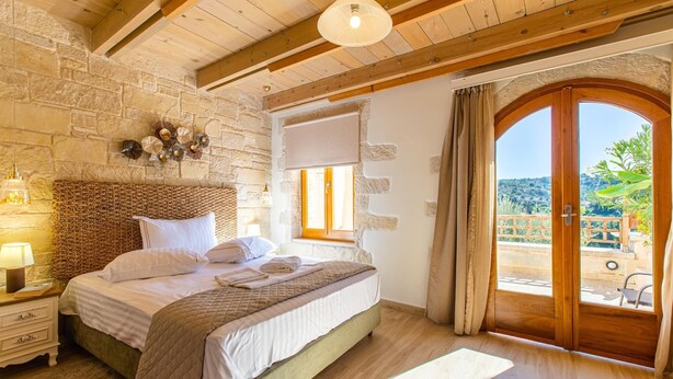Ein Schlafzimmer mit Steinwand, Holzbalken, einem großen Bett, einem Fenster und Blick ins Freie.