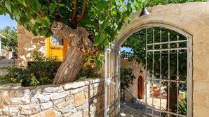 Eine Steinsäule, überwachsen mit einem Baum, die zu einem verschlossenen Eingang mit schmiedeeisernem Tor führt.