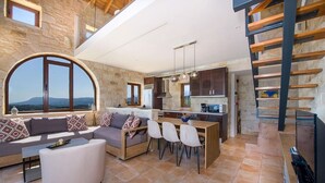 A modern living room with a sofa, dining area, and kitchen. - Cretan Stone Villa, A/C, Private Pool, Spectacular 360° Views of the Countryside, Coastline & Sea! (Stalos)