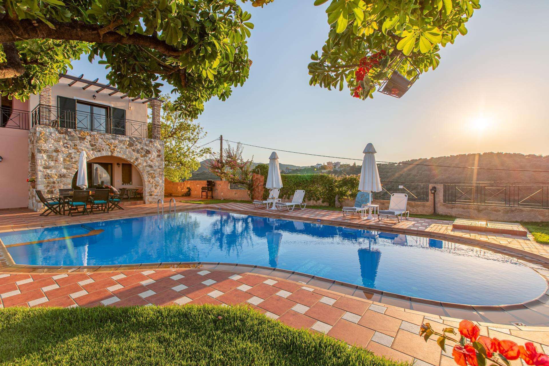 A swimming pool with a stone wall and a patio area with chairs and umbrellas.