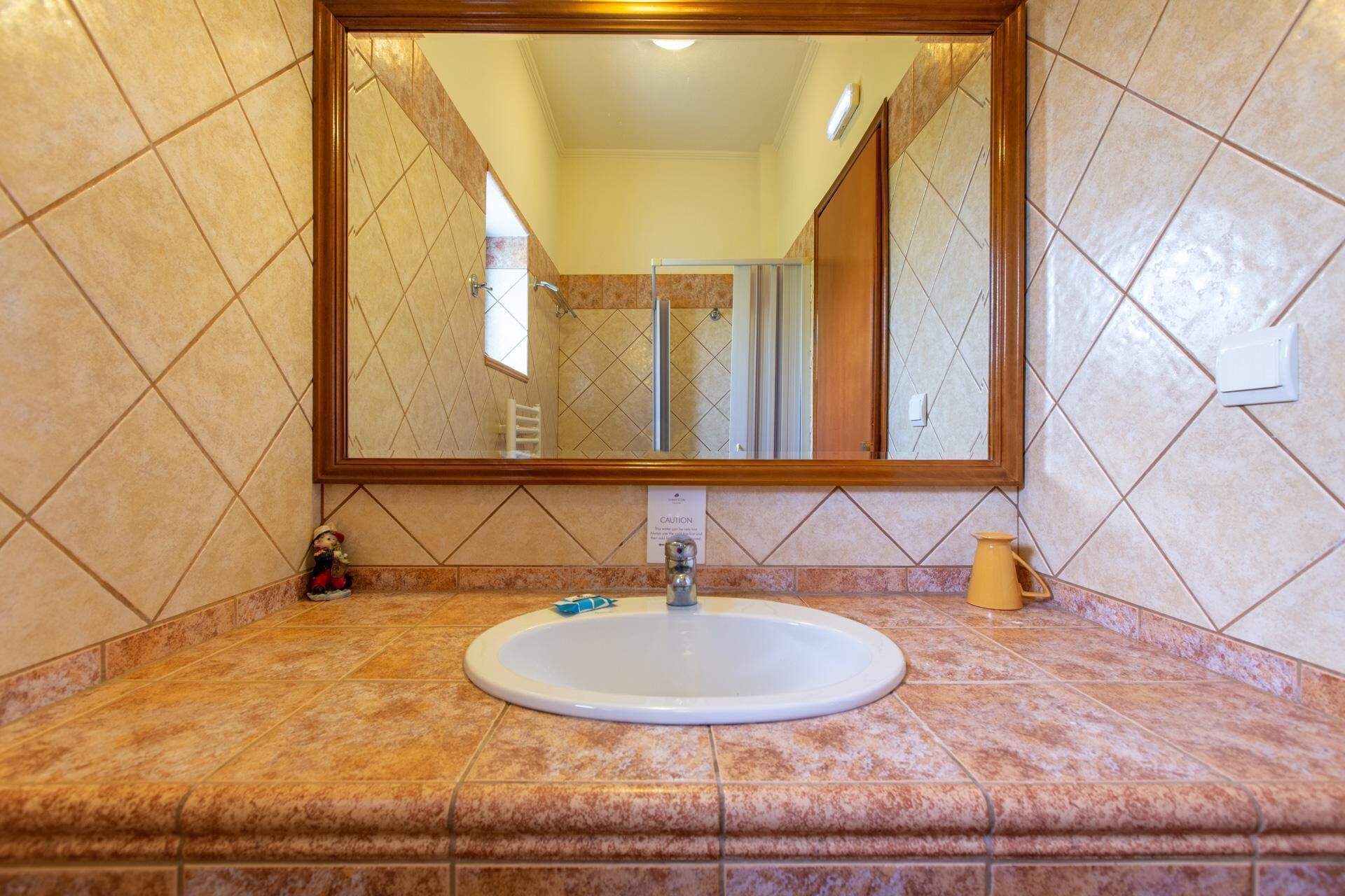 A bathroom with a large mirror, a sink, and a caution sign.