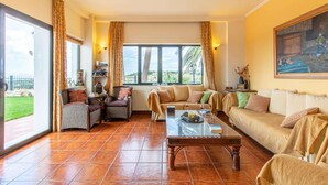 A spacious living room with a large window, a sofa, a coffee table, and a dining area. - Welcoming Family Villa - Private Pool, Stunning Mountain, Countryside & Sea Views close to Beaches! (Stalos)