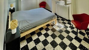 Een slaapkamer met een geruite vloer, een bed, een rode stoel en een raam met gordijnen.