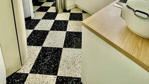 Een keuken met een geruite vloer, witte kastjes, een spoelbak en een waterkoker.