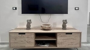 Un salon moderne avec un téléviseur à écran plat fixé au mur, une console en bois ornée de deux statuettes d’ours décoratives, un bol et un meuble à tiroirs doté d’un compartiment dissimulé.