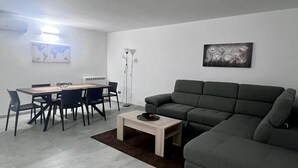 Un salon moderne avec un canapé gris, une table à manger avec des chaises, une table basse et un lampadaire.