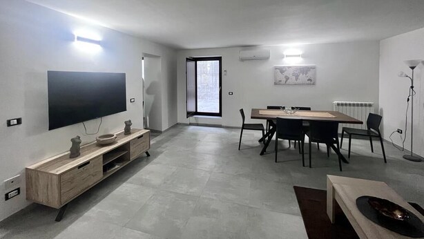 Un salon moderne doté d’un téléviseur à écran plat, d’un meuble TV en bois, d’une table à manger avec des chaises et d’une grande fenêtre.