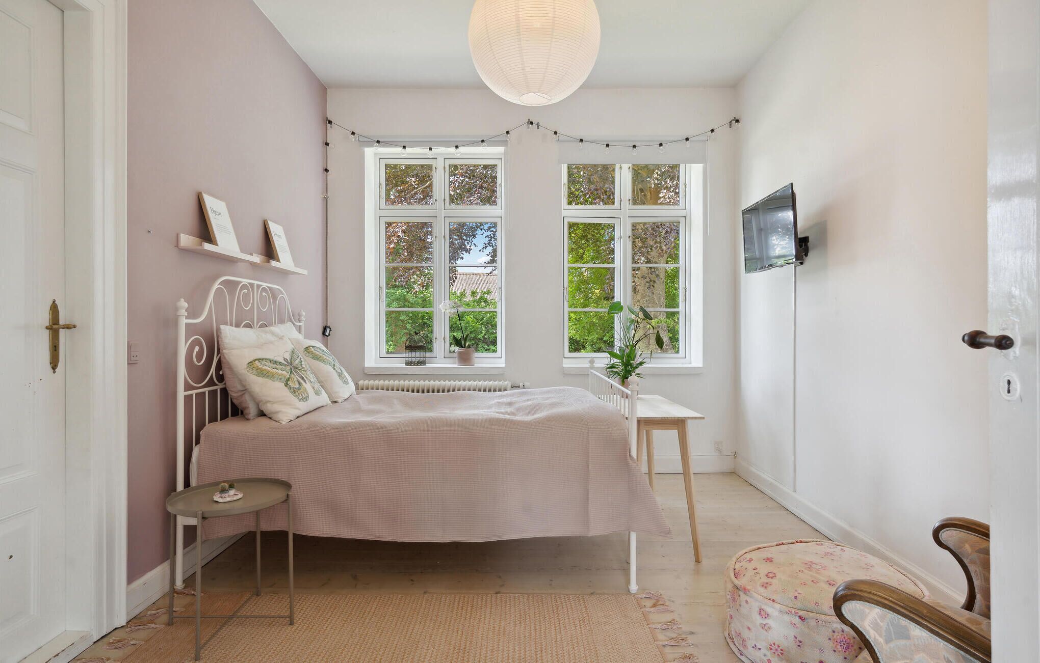 A bedroom with a bed, bedside table, chair, and a TV mounted on the wall.