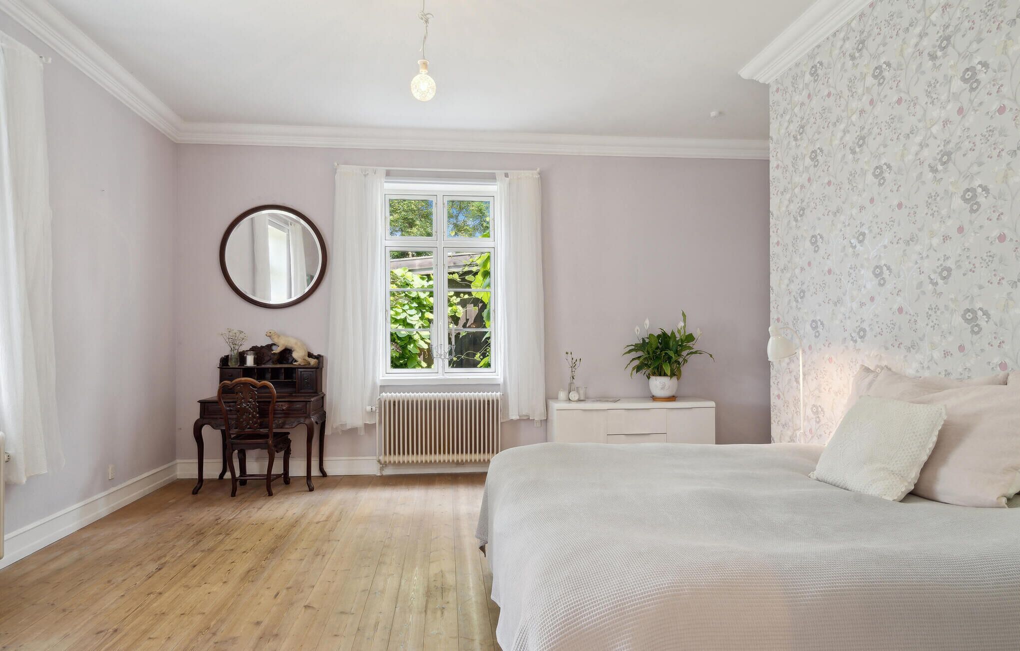 Une chambre à coucher avec un grand lit, une commode, un miroir et une fenêtre donnant sur un paysage verdoyant.