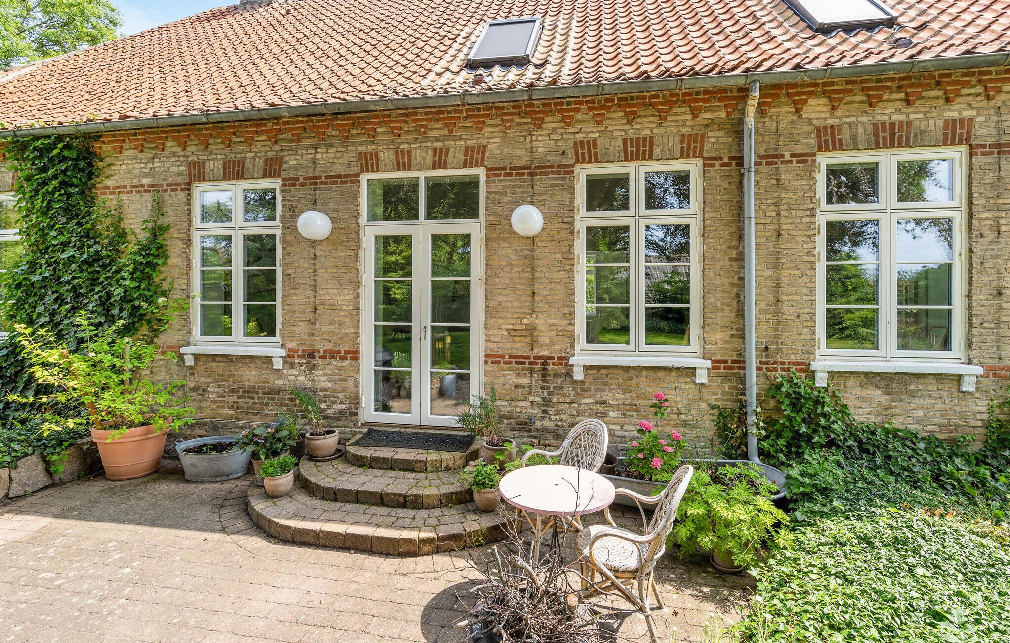 A brick house with a tiled roof, large windows, and a small patio with a table and chairs.