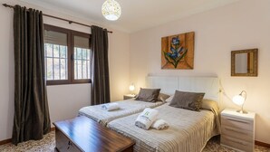 A hotel room with two beds, a wooden bench, a painting, and a nightstand with a lamp. - Casa de la Cruz Iznájar by Ruralidays (Córdoba)