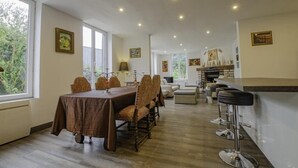 Un grand espace dédié à la salle à manger, avec une longue table et des chaises, un bar avec des tabourets et une cheminée.