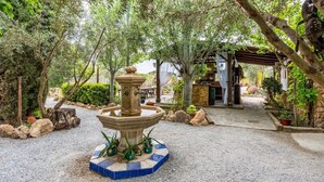 Un jardín con una fuente de piedra, rodeado de árboles y plantas en macetas.