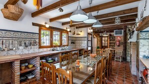 Una cocina rústica con vigas de madera, una larga mesa de comedor y utensilios de cocina colgando.
