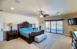 A bedroom with a large bed, a ceiling fan, a TV, and a view through a sliding glass door.