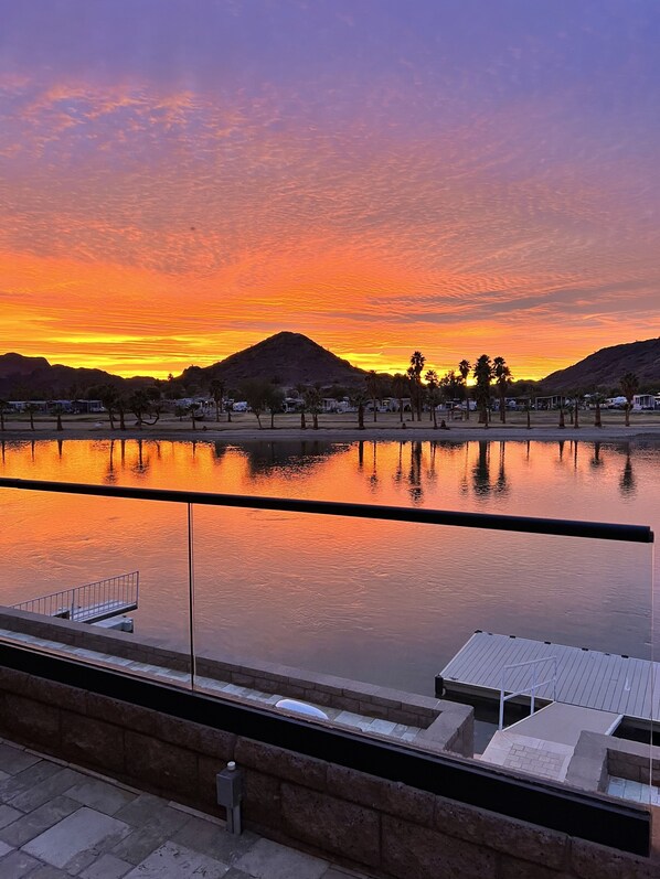 A sunset view over a calm body of water with a dock and a stone wall in the foreground.