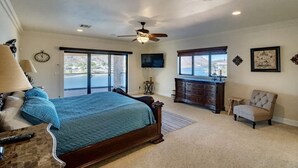 A bedroom with a large bed, a ceiling fan, a TV, a dresser, a chair, and a view of the outdoors.