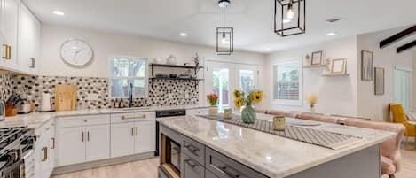 A modern kitchen with white cabinetry, a large island, and a clock on the wall.