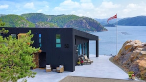 Un bâtiment moderne de couleur noire, doté d’un balcon donnant sur un plan d’eau et des montagnes.