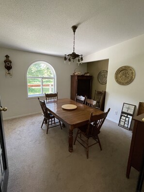 A dining room with a wooden table, chairs, a chandelier, a clock, and a window with a view of greenery. - Old Cowboy Ranch Guesthouse - CALL FOR AVAILABILITY (Westbridge)