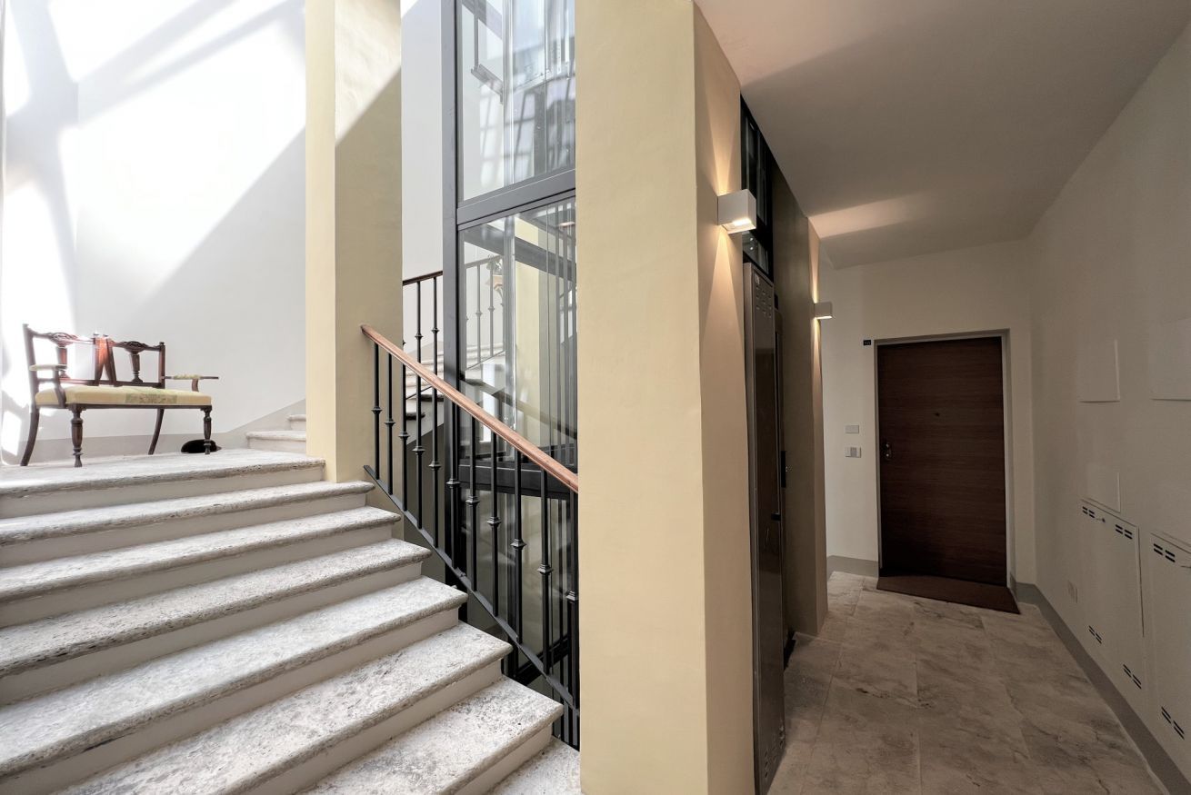 A modern staircase with a glass railing, leading to an elevator.