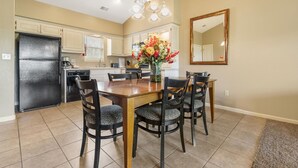 A dining area with a wooden table and chairs, a vase of flowers, and a kitchen in the background. - Cozy & Charming Condo at StoneBridge Village Resort (Reeds Spring)