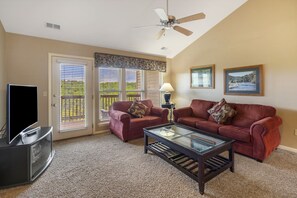 A living room with a TV, two red sofas, a glass coffee table, and a ceiling fan.