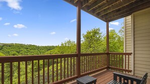 Una terraza de madera con banco y mesa, con vistas a una zona boscosa.