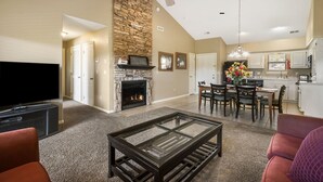 A living room with a fireplace, a television, and a dining area with chairs and a table. - Golf Condo for Two at Beautiful StoneBridge Village Resort (Reeds Spring)