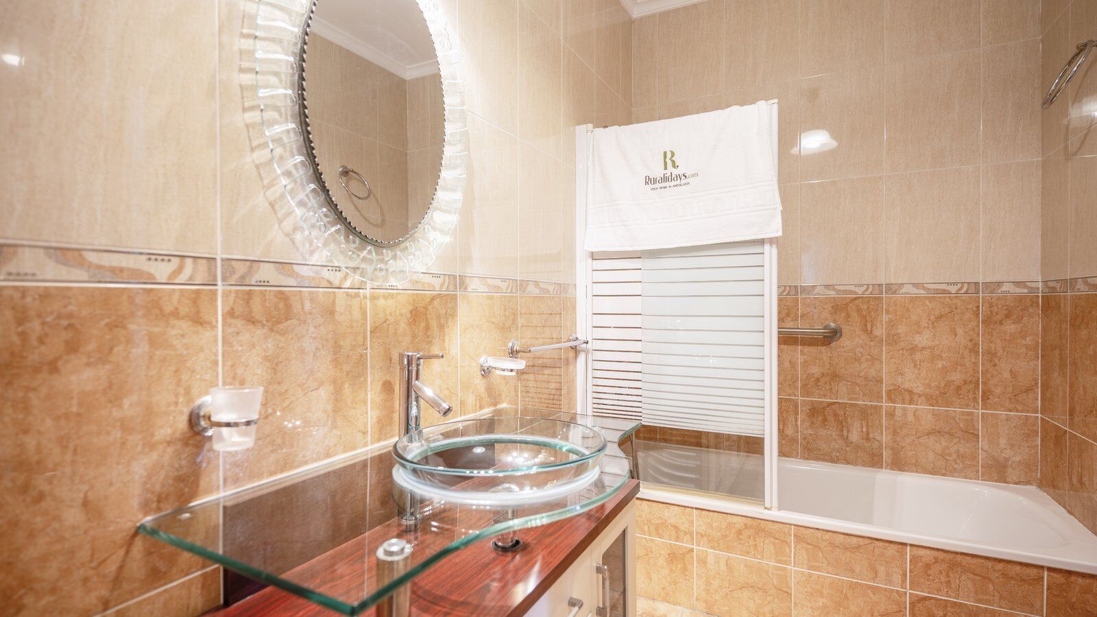 A bathroom with a glass sink, a round mirror, a white towel, and a bathtub.