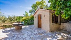 Une terrasse en pierre avec une table en pierre et un petit bâtiment doté d’une porte et d’une fenêtre en bois.