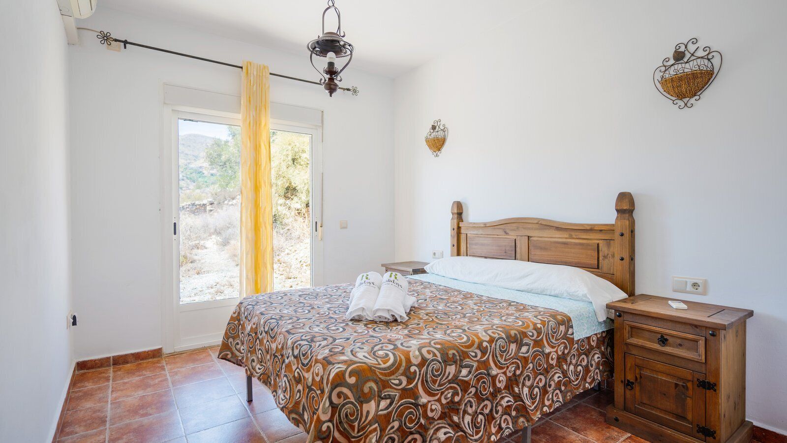 A bedroom with a bed, wooden nightstand, and a window with curtains.