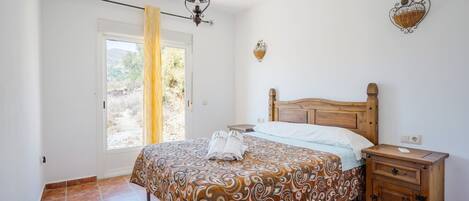 A bedroom with a bed, wooden nightstand, and a window with curtains.