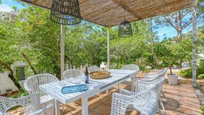 Een terras buiten met een witte tafel en rieten stoelen, omgeven door groen.