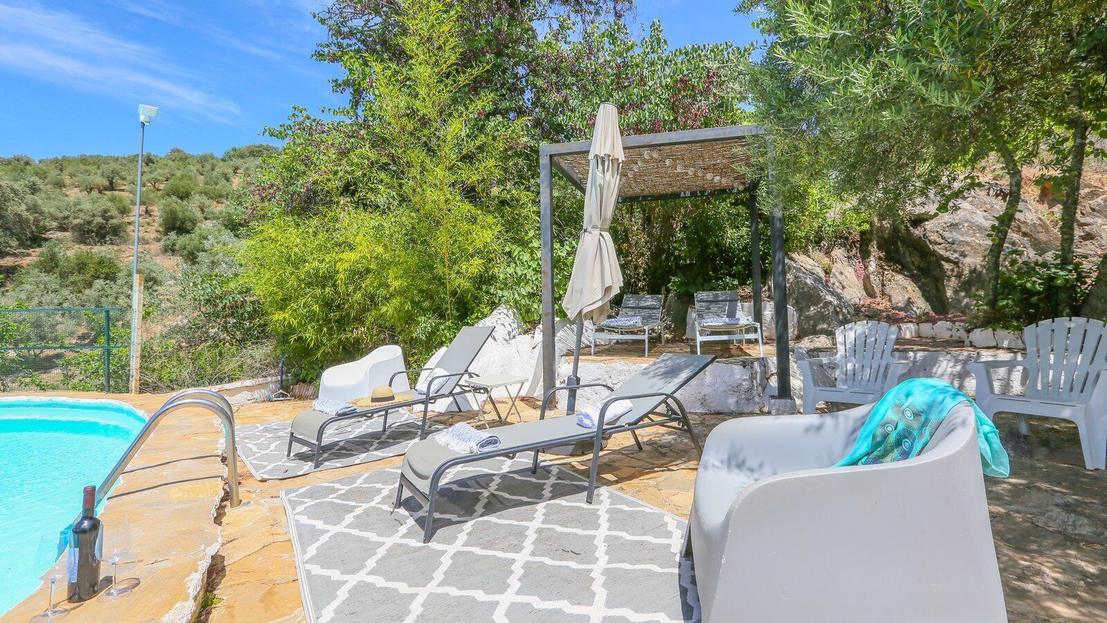Un espace aménagé au bord de la piscine, avec des chaises longues, une pergola et une vue dégagée sur le paysage environnant.