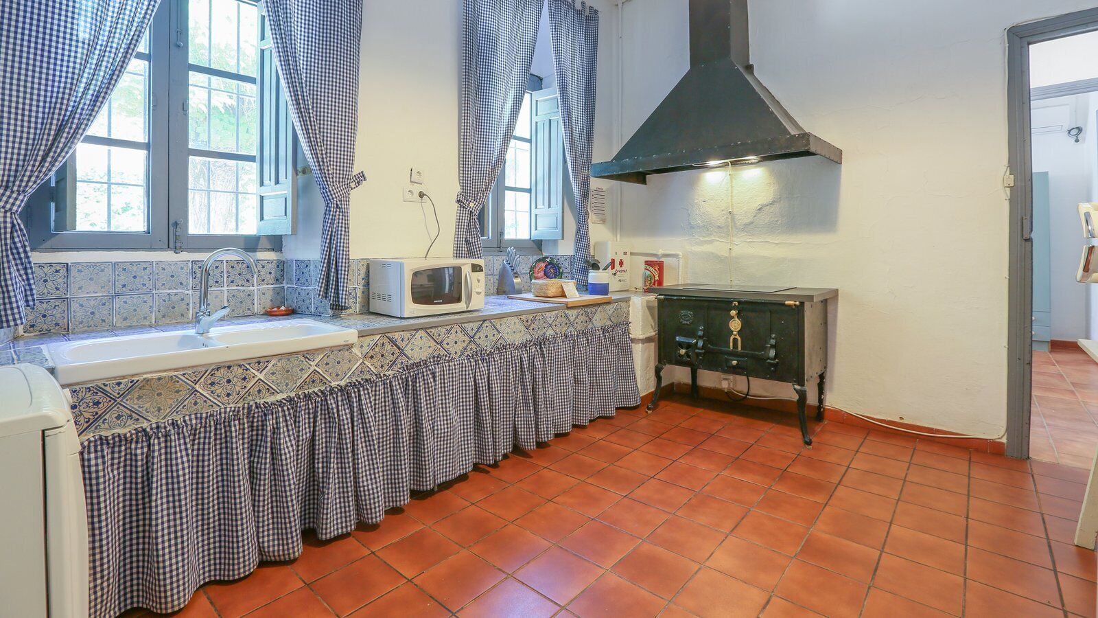 Cucina con schienale piastrellato, lavello, forno a microonde, fornello e cappa aspirante nera.