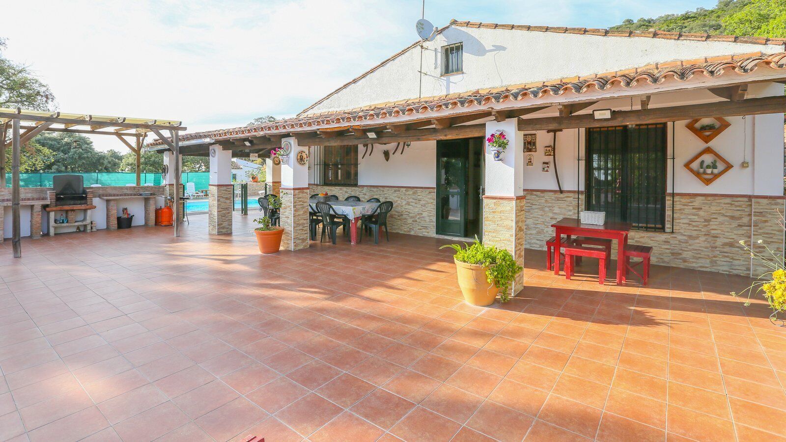 A covered patio area with a barbecue setup, outdoor seating, and potted plants.