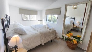 Una camera da letto con un letto, una lampada da comodino, uno specchio e una finestra vista alberi.