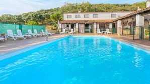 Una piscina con lettini, un edificio con tetto in tegole e un recinto verde sullo sfondo.