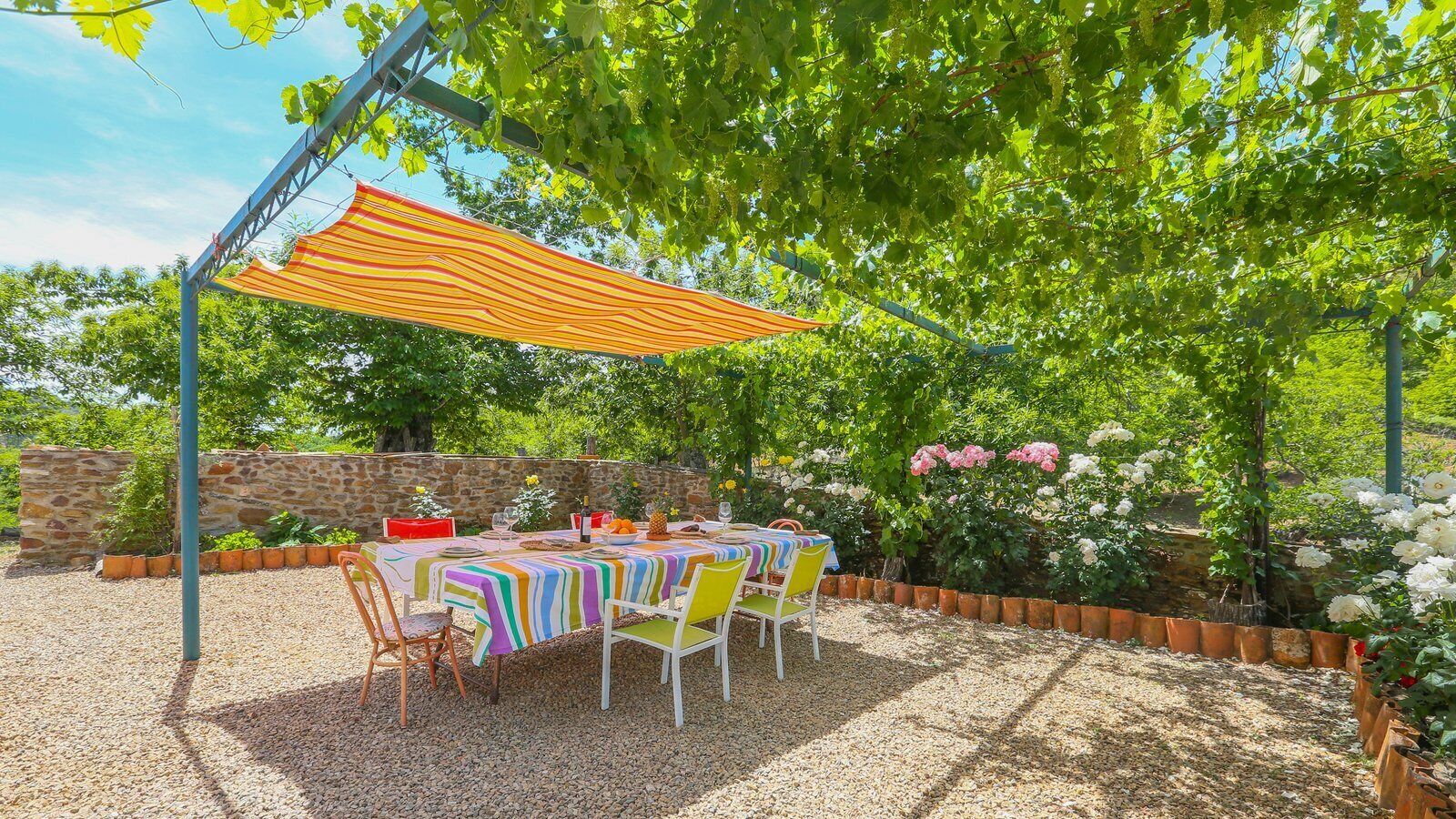 Une terrasse extérieure avec une table dressée pour le repas, entourée d’un mur de pierre et d’une végétation luxuriante.