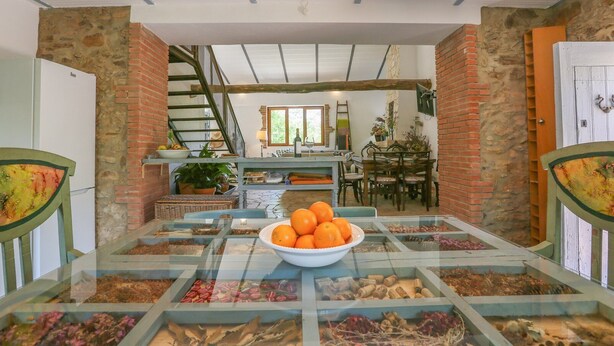 Un coin repas avec une table à plateau de verre sur laquelle sont disposés divers aliments, un bol d’oranges et un escalier menant à un niveau supérieur.