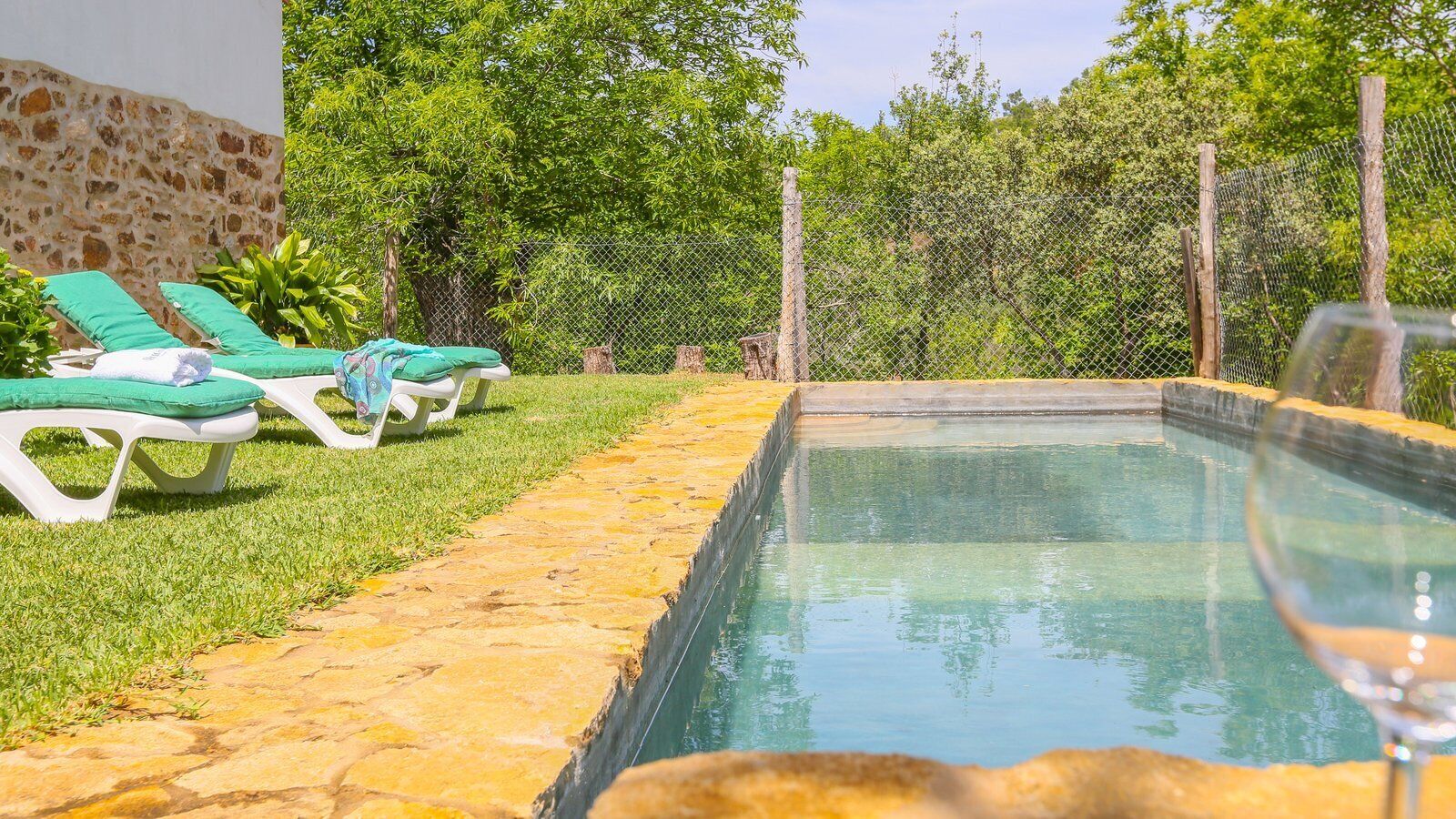A swimming pool with a stone border, surrounded by a grassy area and a stone wall.