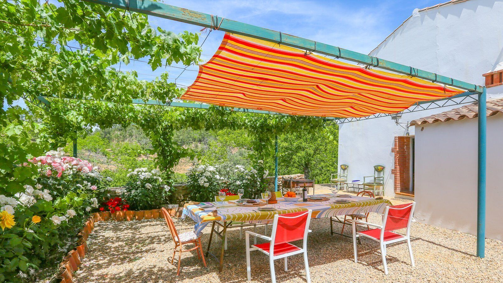 An outdoor dining area with a table set for four, surrounded by red and white chairs, under a striped awning.